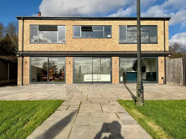 Two storey rear extension in pale brick with full-width glazing and a paved path