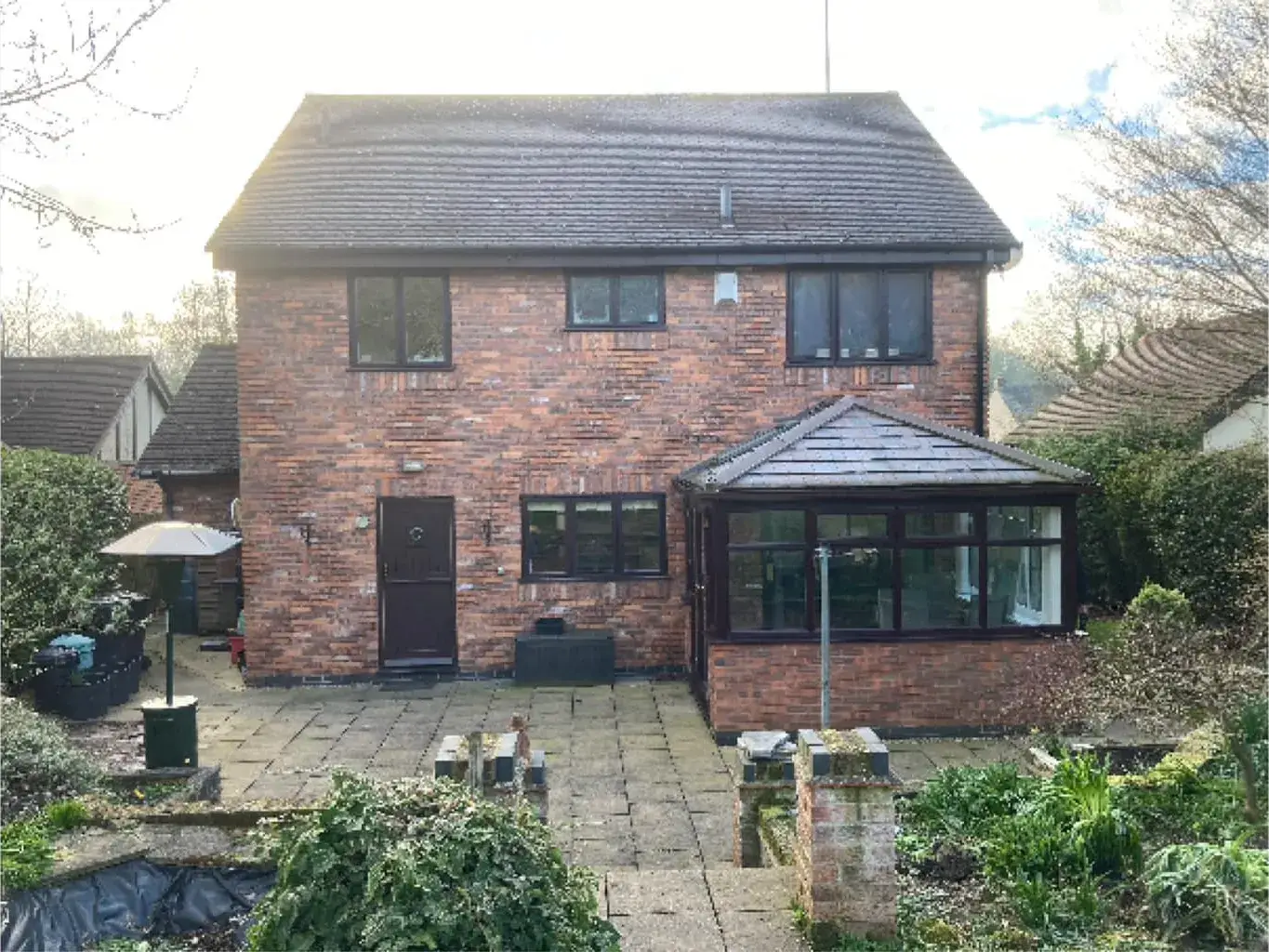 Rear of a detached house before work, with a dated conservatory and paved patio