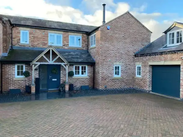 Detached brick house with an oak-framed porch, blue front door and block-paved driveway